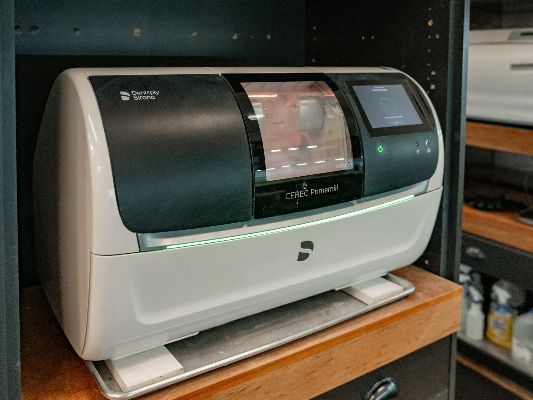 A dental milling machine sits on a wooden shelf, ready for use with a touchscreen display.