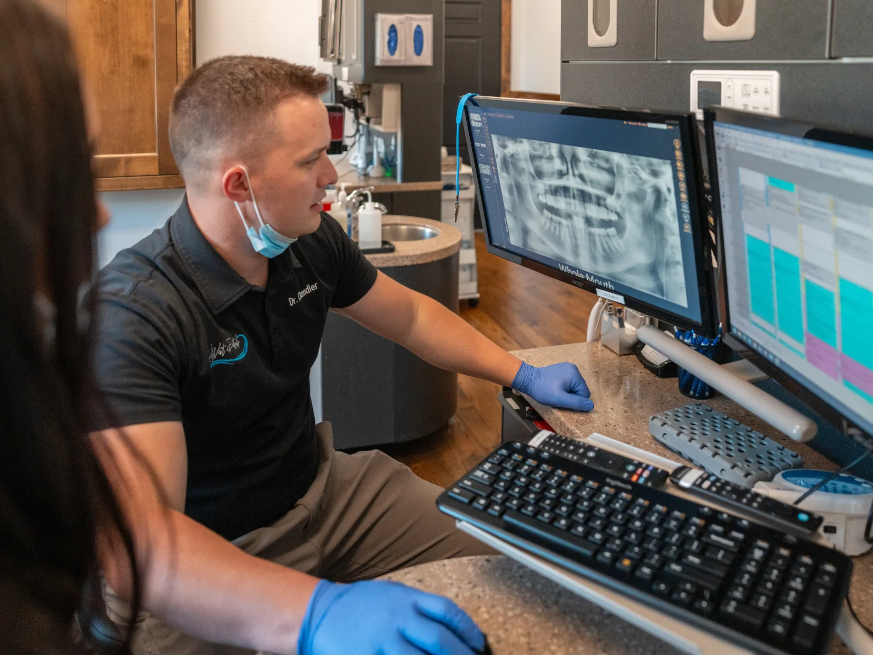 A dentist reviews a dental X-ray on a computer screen while discussing with a patient.