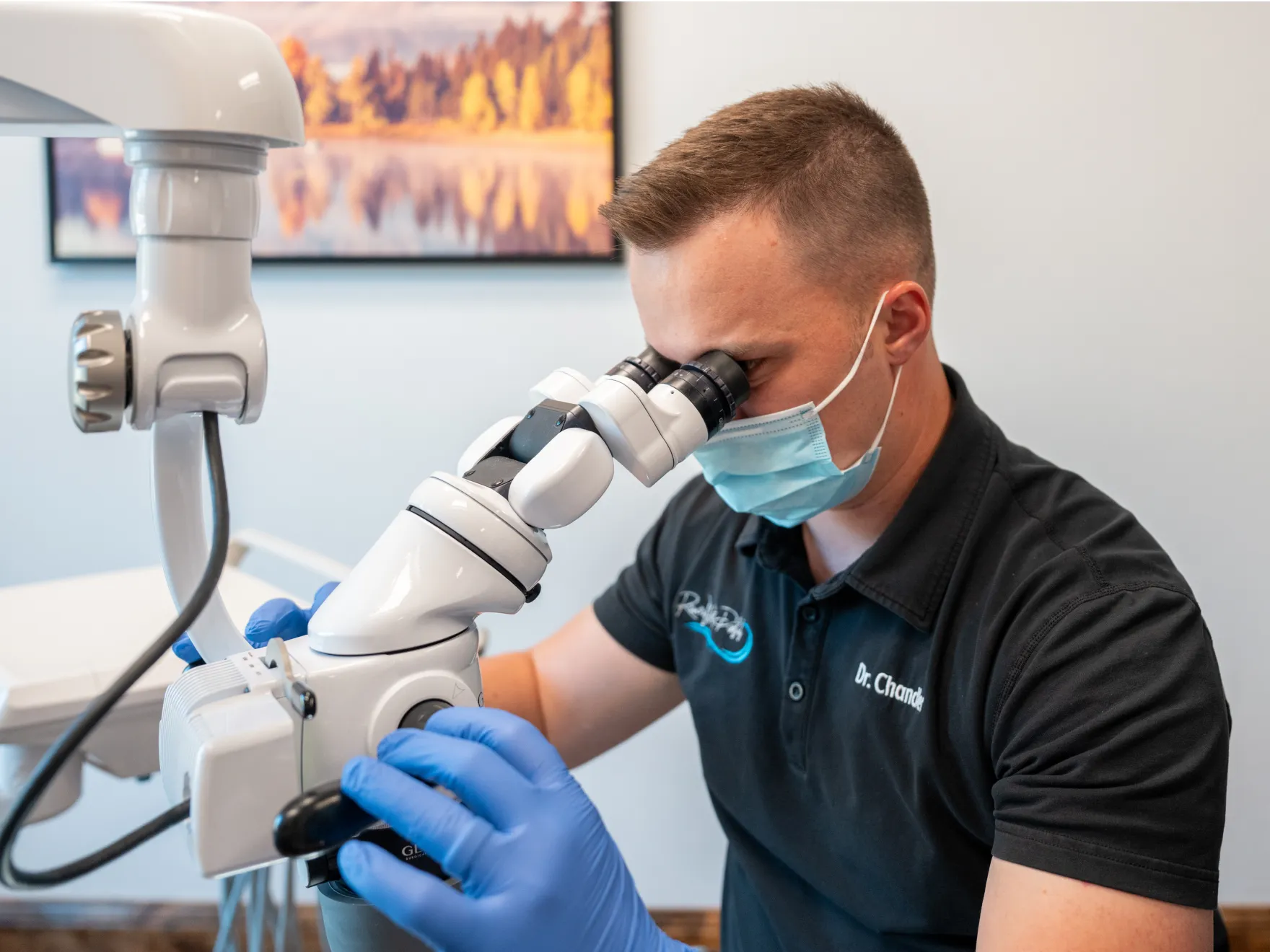 A person in gloves and mask uses a microscope for close examination.